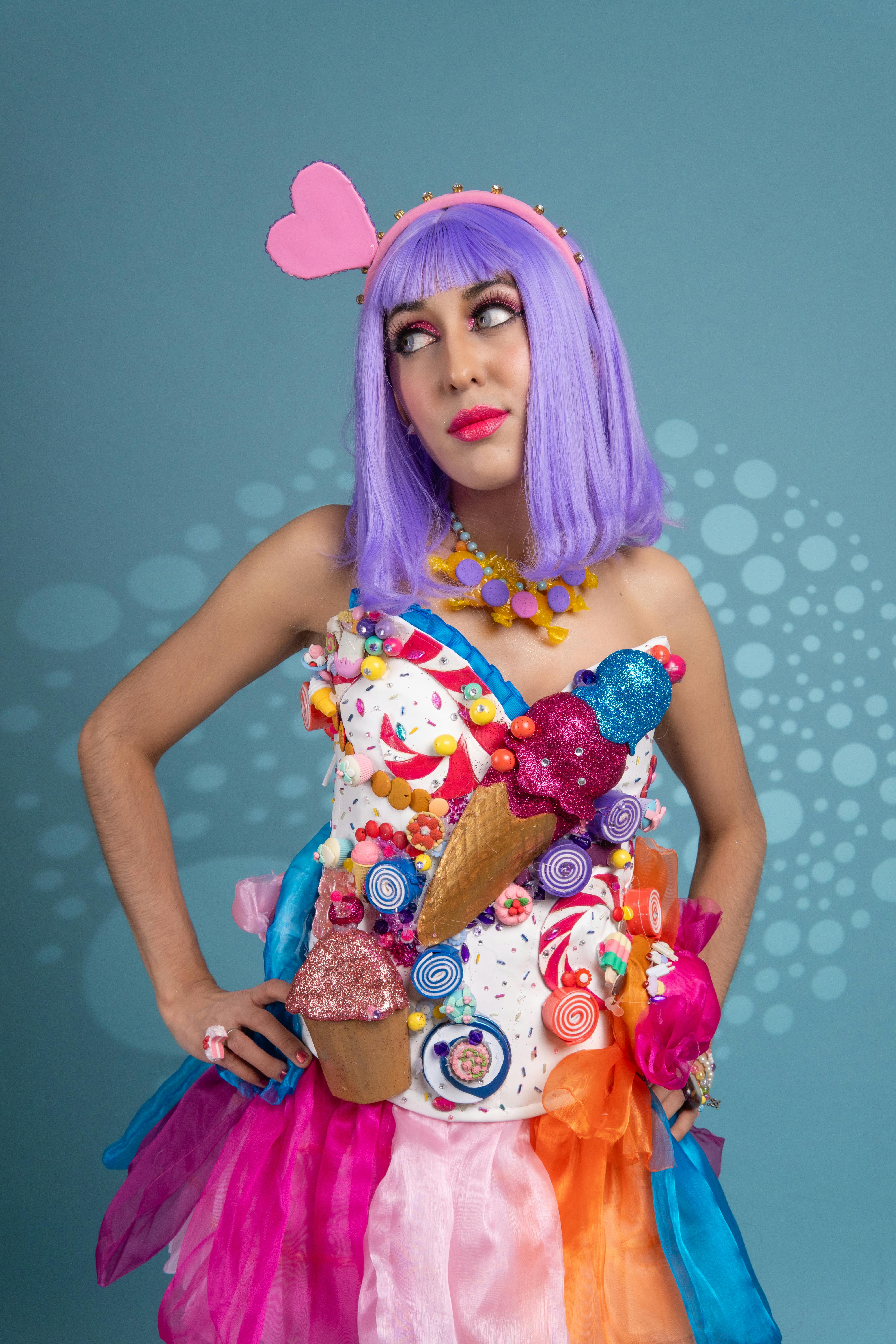 ingyenes Fiatal nő színes, cukorka témájú cosplay ruhában, lila parókával és szíves fejpánttal kék háttérrel. Stockfotó