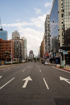 Wide city street lined with modern and classic buildings under a blue sky.