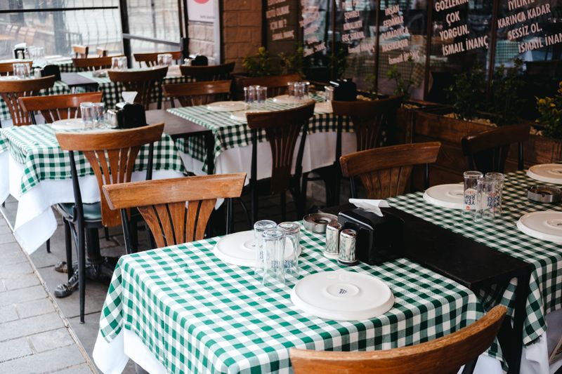 Charming café interior with checkered tablecloths and empty wooden chairs, ready for service.