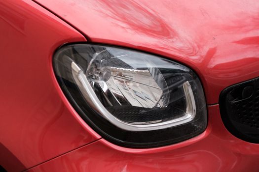 Detailed view of a shiny red car's headlight showcasing modern automotive design.