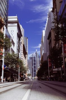 Dynamic view of a bustling Sydney street lined with modern skyscrapers under a vivid blue sky.
