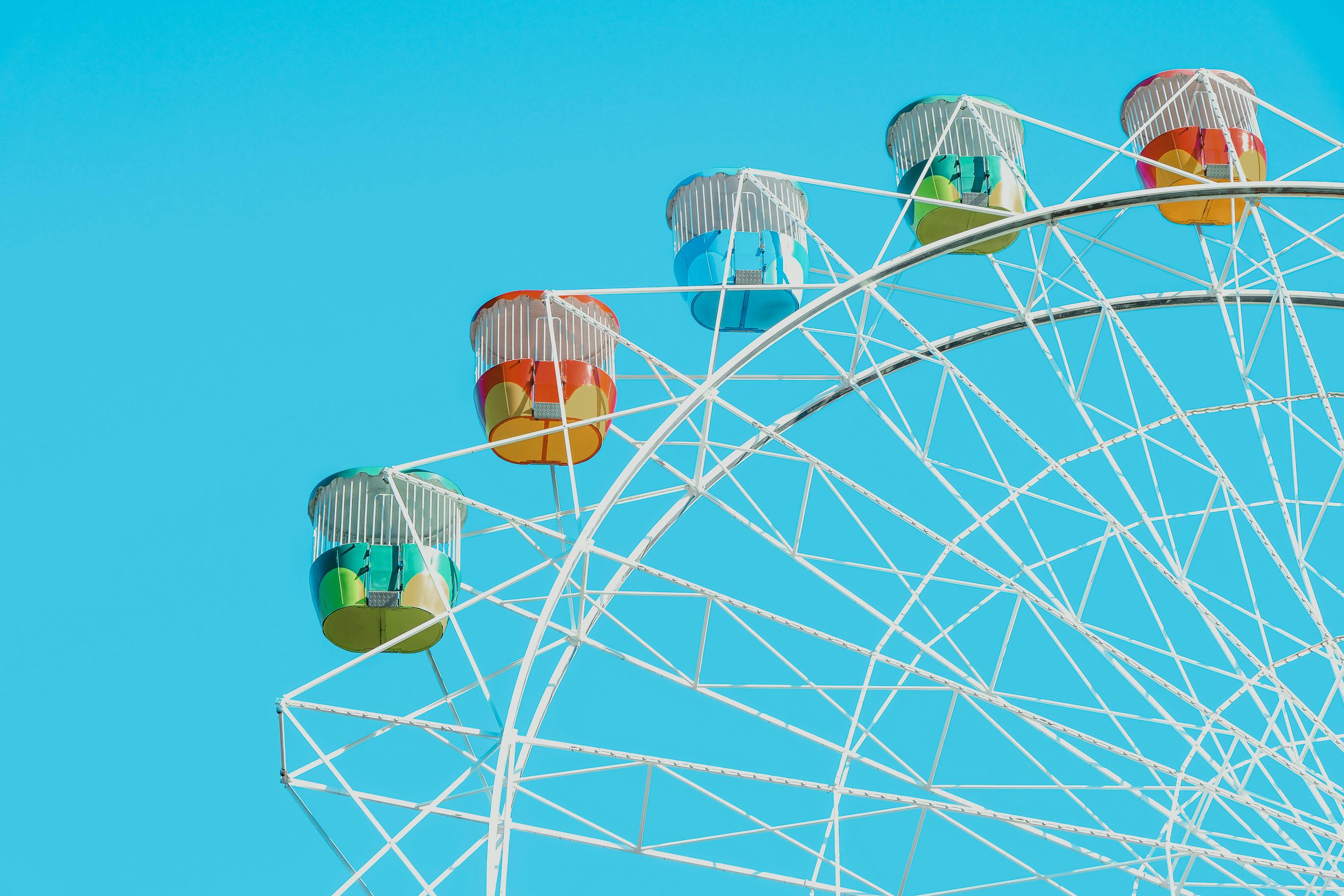 Bright and colorful Ferris wheel with vibrant cabins set against a clear blue sky.
