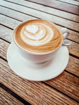 A cappuccino with heart-shaped latte art on a wooden table, perfect for cozy cafe vibes.