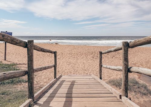 Free Serene view of a beach with a wooden walkway leading to the ocean under a clear sky. Stock Photo