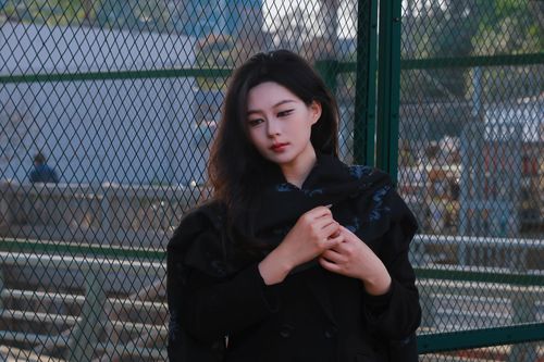 Free A young woman in a thoughtful pose by a city fence, expressing urban mood. Stock Photo
