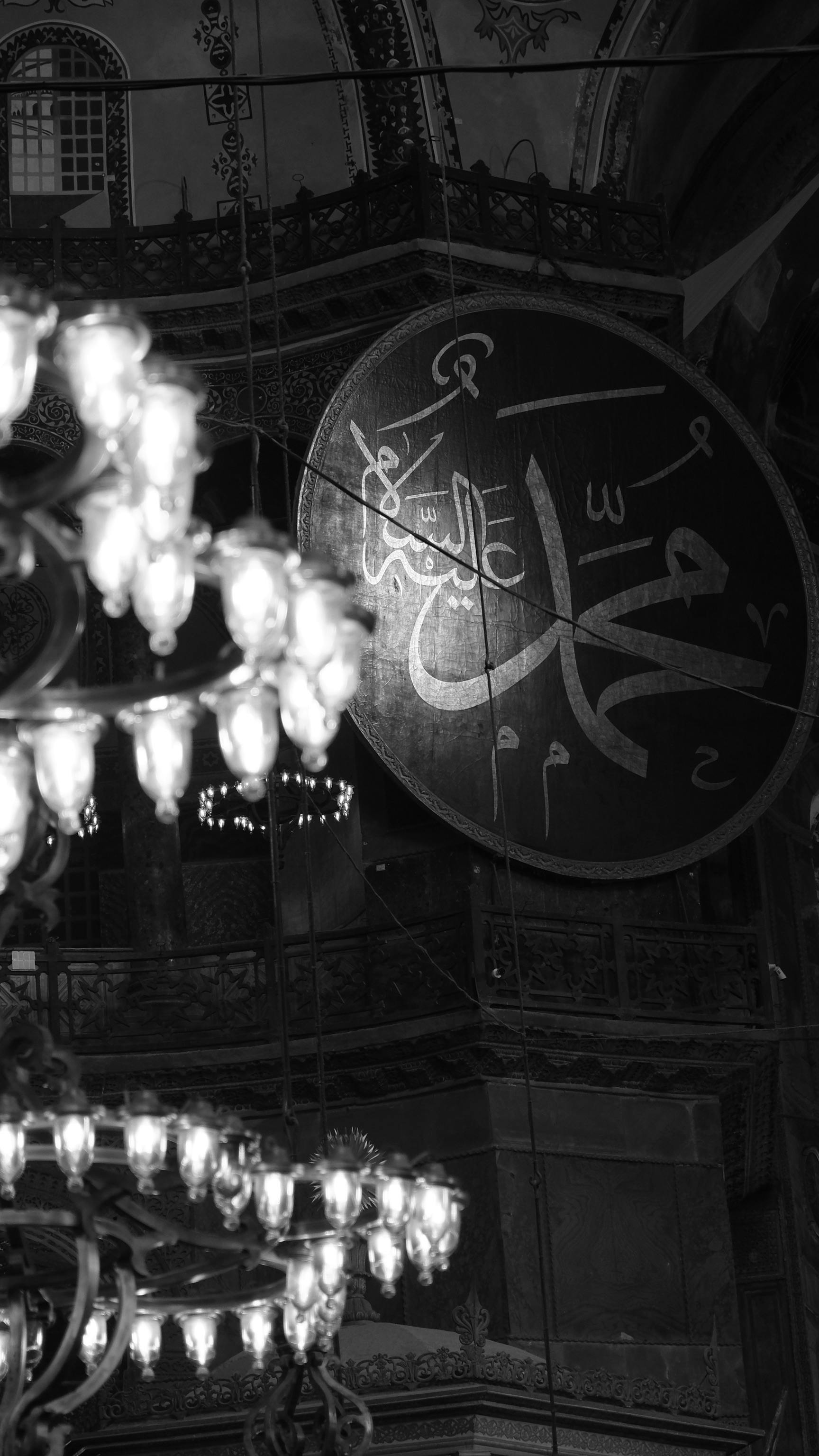Free Monochrome photo of mosque interior featuring ornate chandelier and Arabic calligraphy. Stock Photo