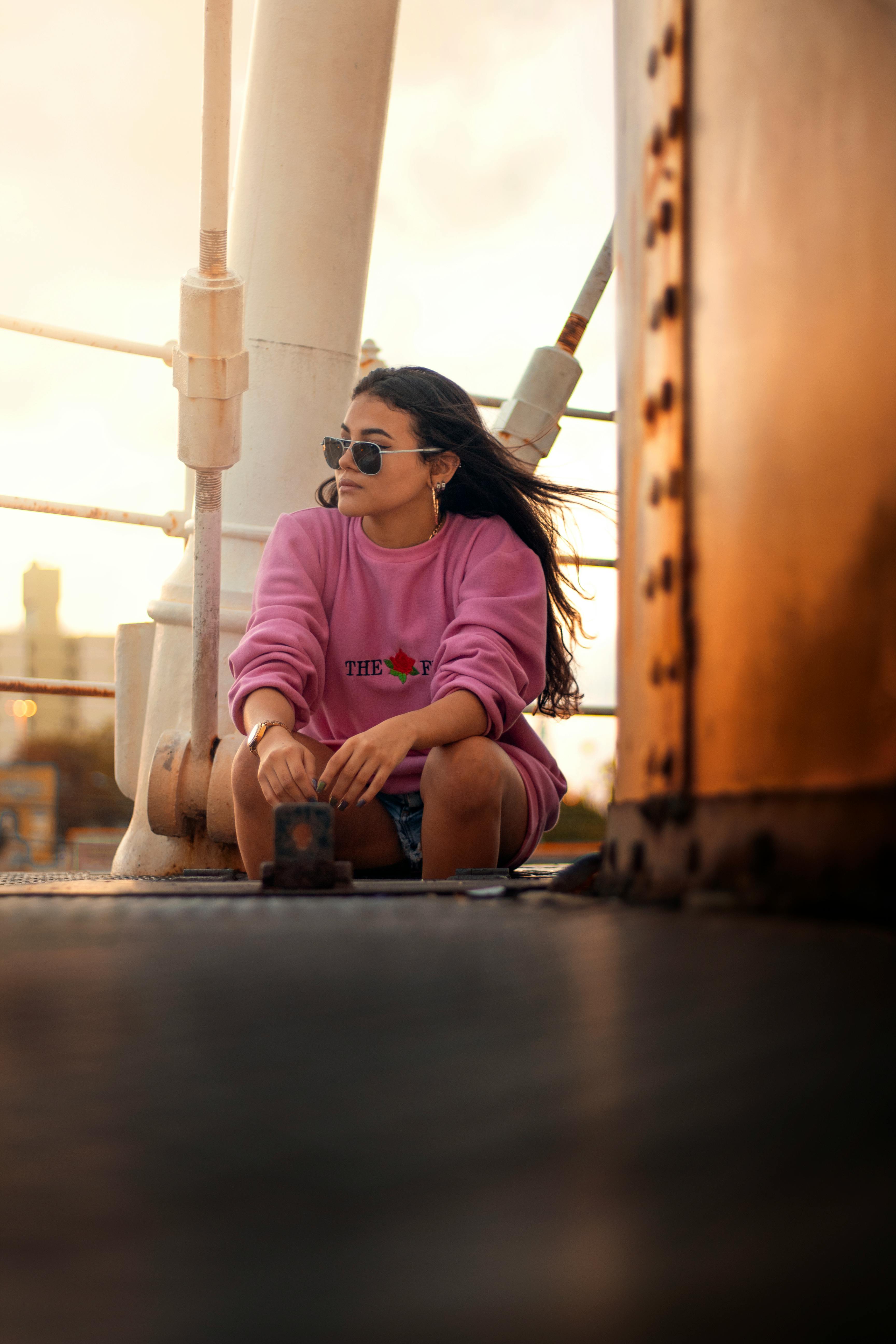 日落时分的桥上，一位穿着粉色毛衣的时尚女性坐着，拥抱休闲与时尚