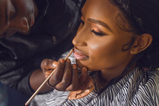 Detailed close-up of a makeup artist applying lipstick to a bride's lips, showcasing precision and artistry.