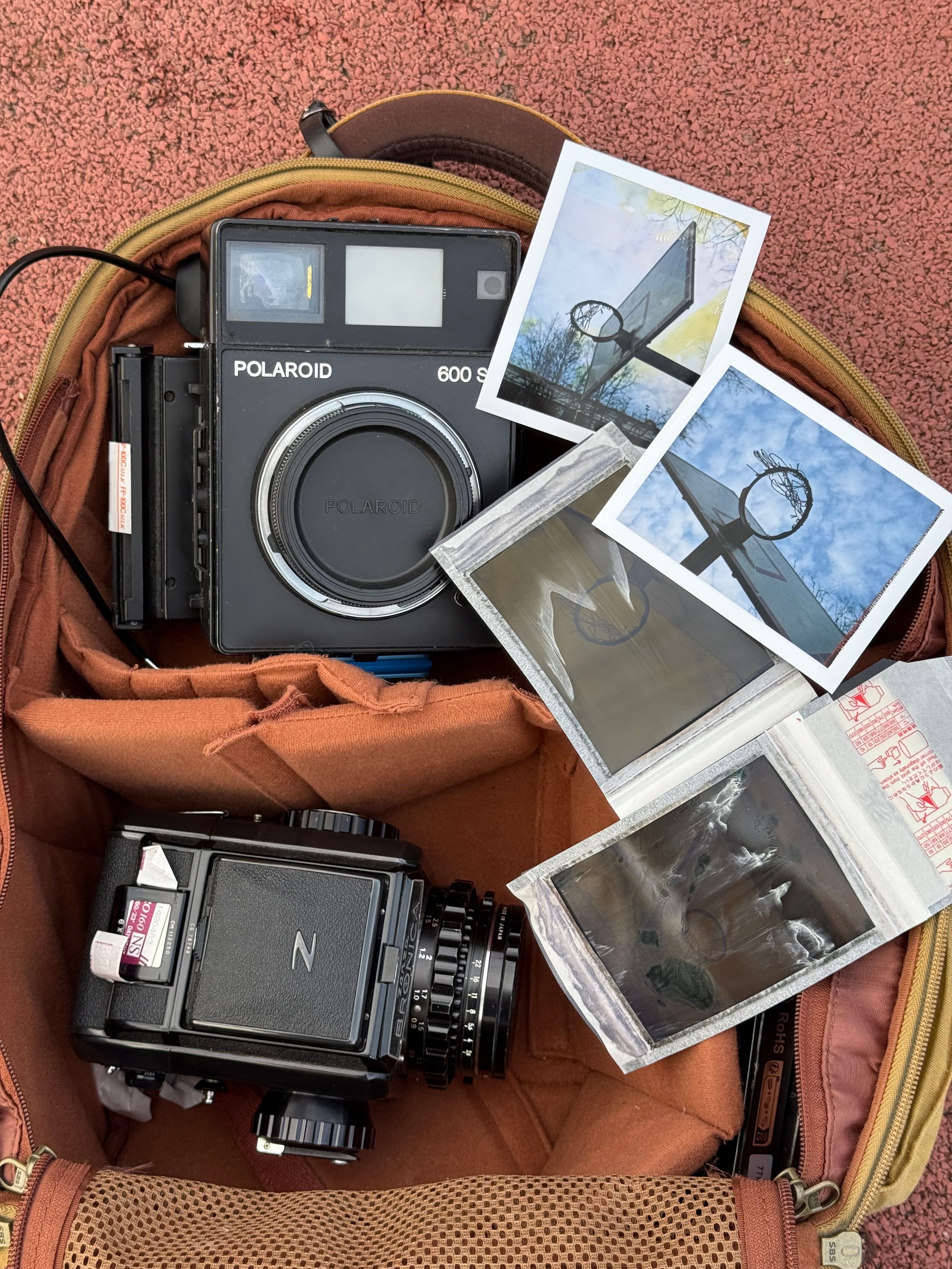 Top view of vintage cameras and Polaroid photos in an open backpack.