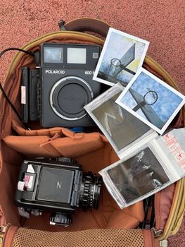 Top view of vintage cameras and Polaroid photos in an open backpack.