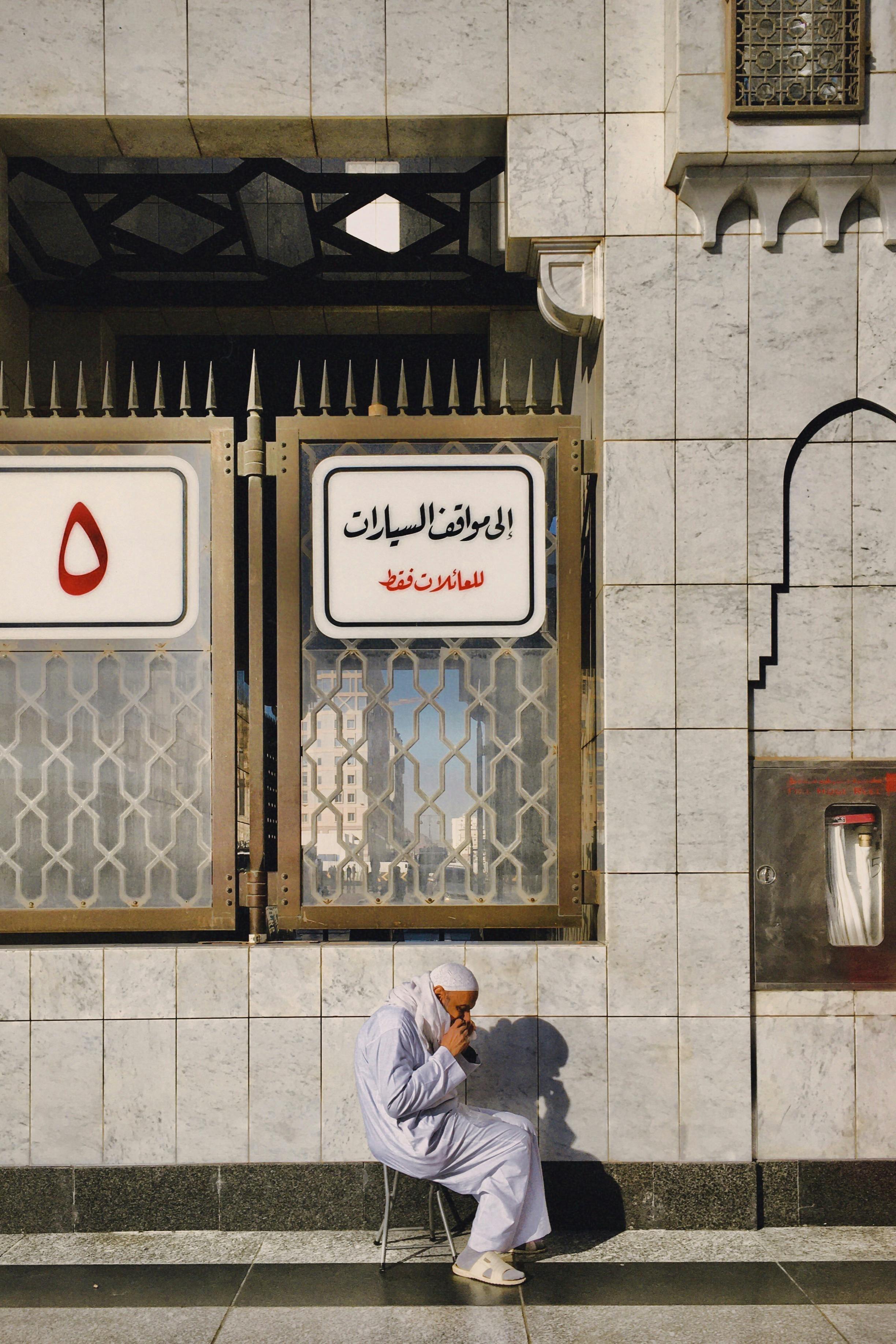 Gratuit Un bărbat în vârstă stă în contemplație lângă semnele arabe de pe exteriorul unei moschei. Fotografie de stoc