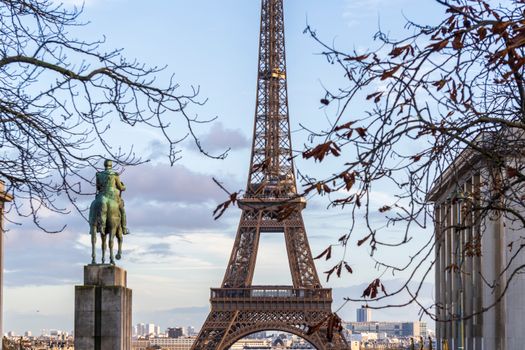 A scenic view of the Eiffel Tower in Paris with a statue and bare tree branches.
