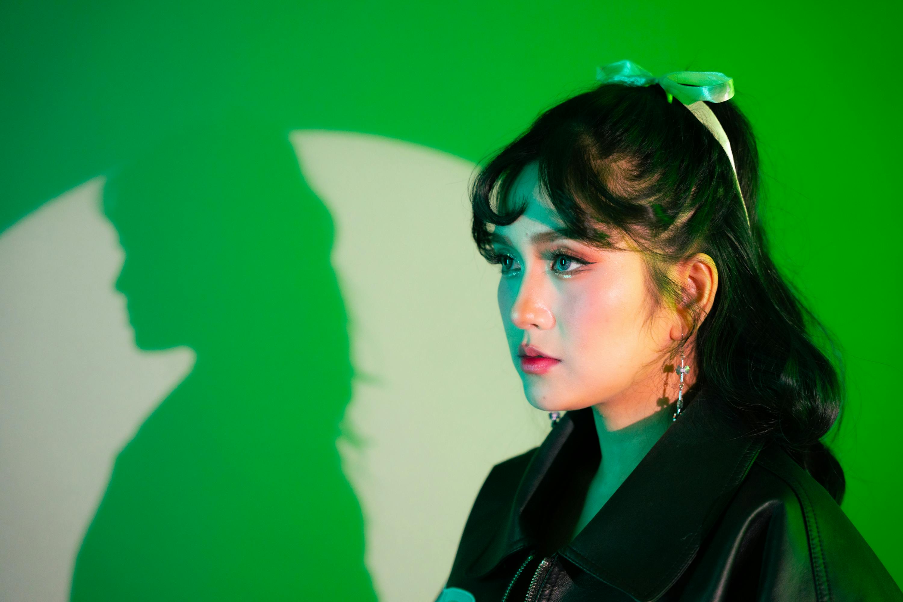 A woman in profile with vibrant lighting and bold shadow against a green background.