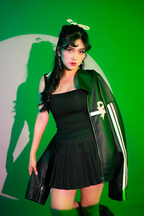 Free Fashionable woman in a black dress and leather jacket posing under green spotlight. Stock Photo