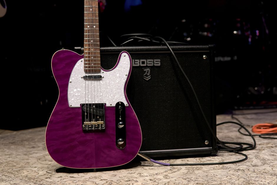 Vibrant purple electric guitar next to amplifier on stage, ready for a performance.