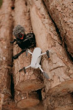 Aerial drone and camera with microphone resting on logs outdoors.