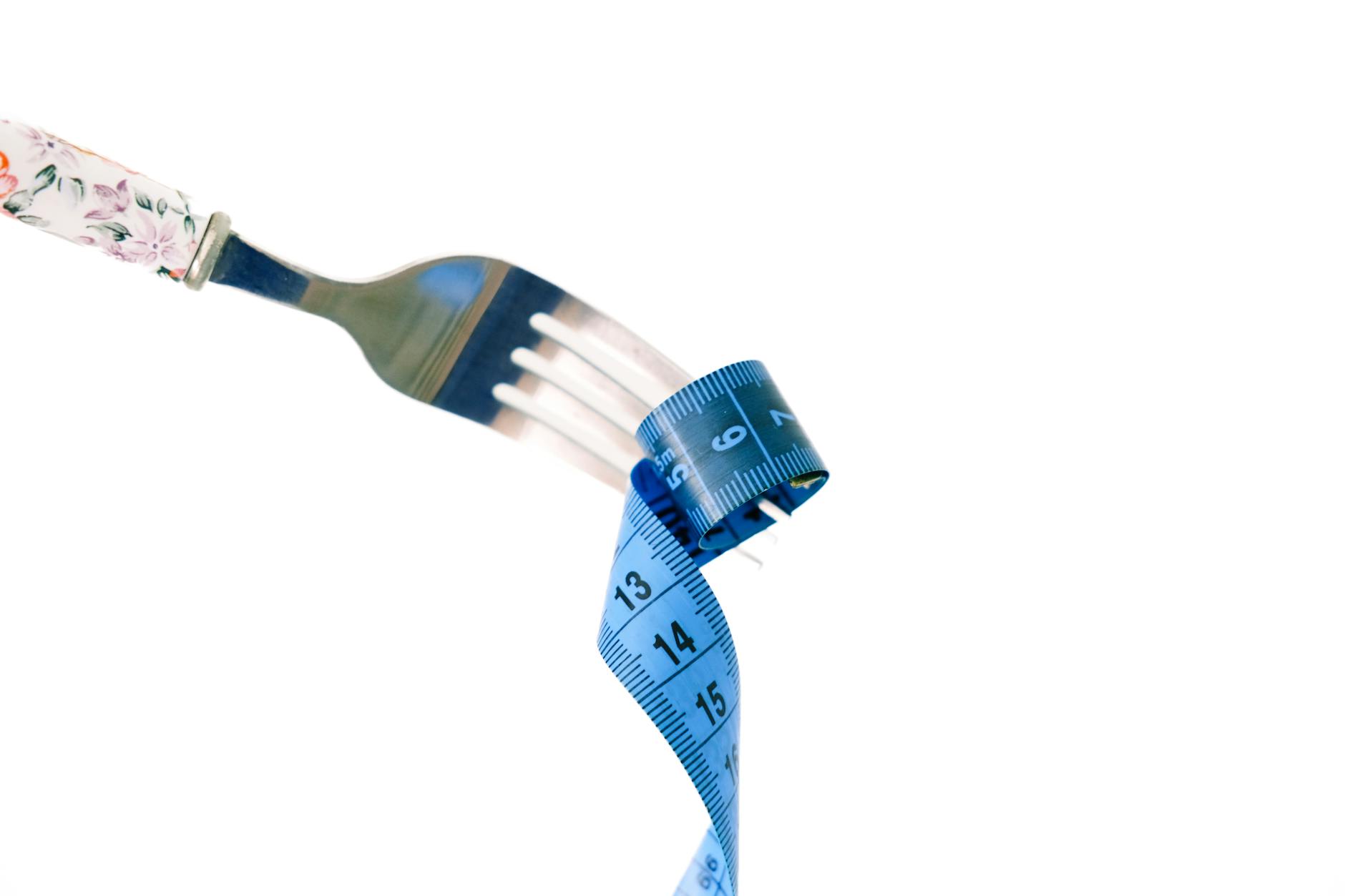 How Long Should You Fast for Weight Loss? A fork twirls a blue measuring tape, symbolizing weight management and health.How Long Should You Fast for Weight Loss?