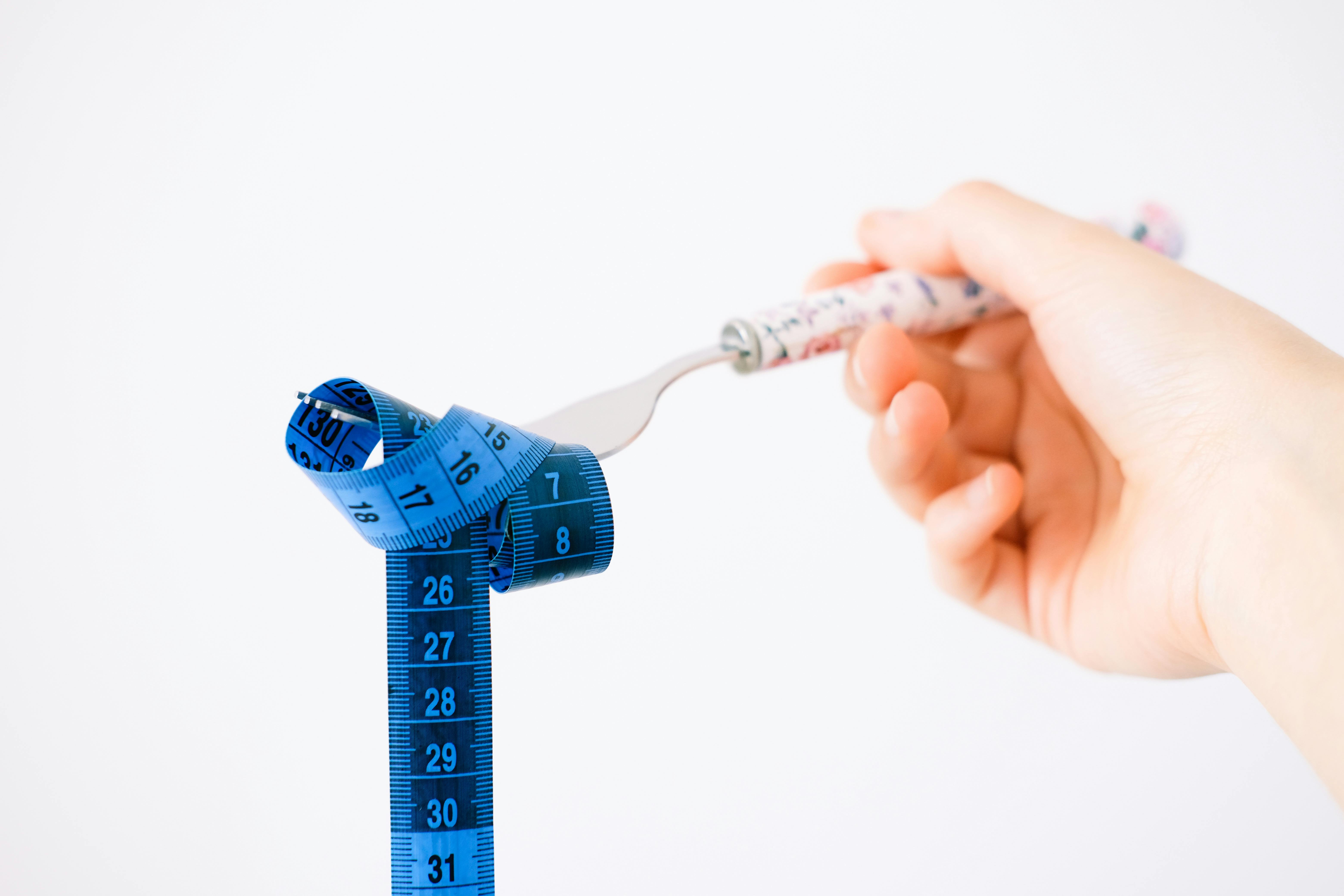 A hand holding a fork wrapped with a blue measuring tape suggesting diet or weight management.