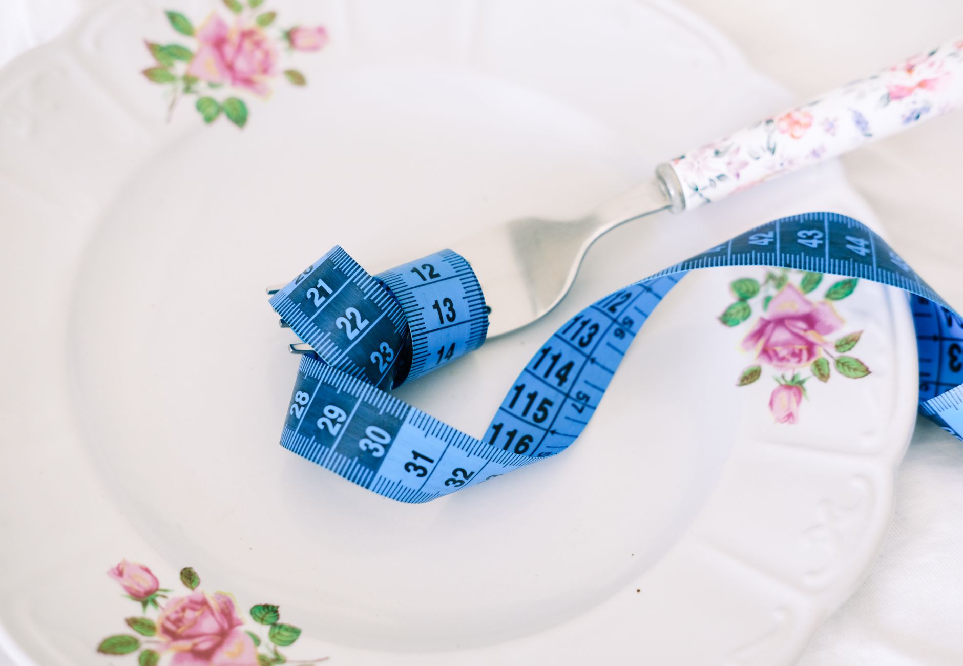 A floral plate with a fork and blue measuring tape symbolizing dieting or healthy eating.