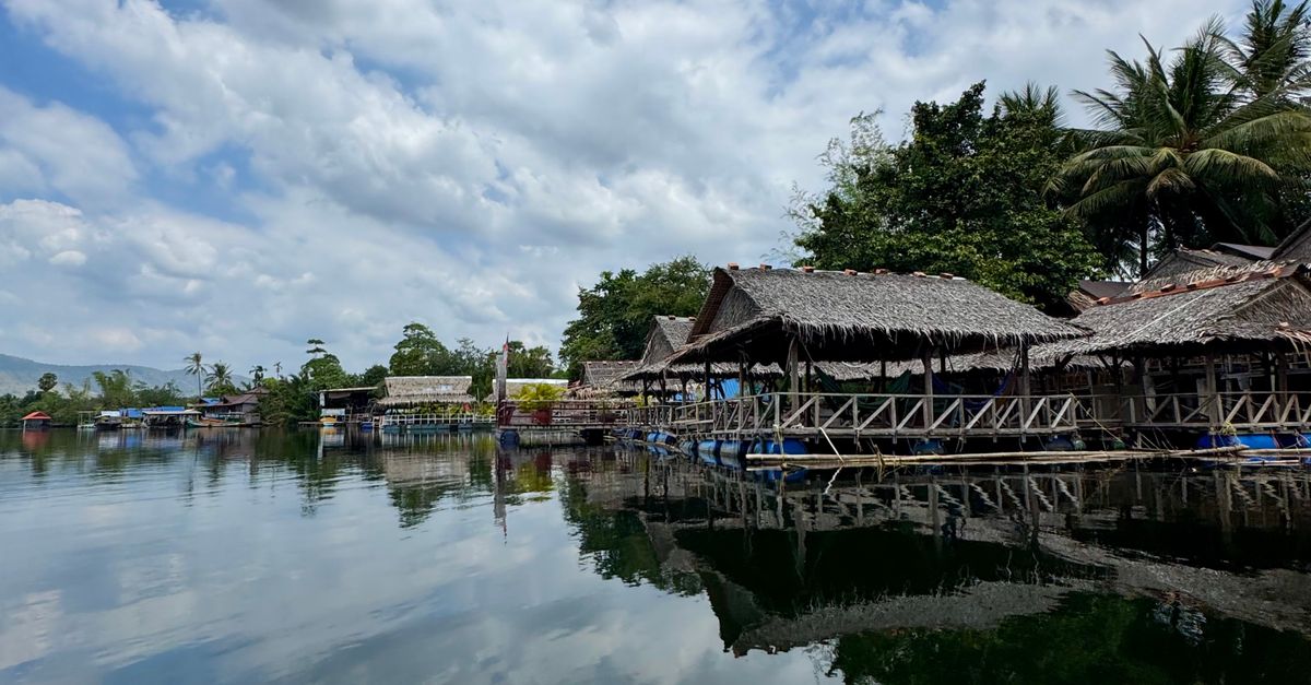 Charming riverside huts with clear reflections in Kampot, Cambodia, under a vibrant sky.