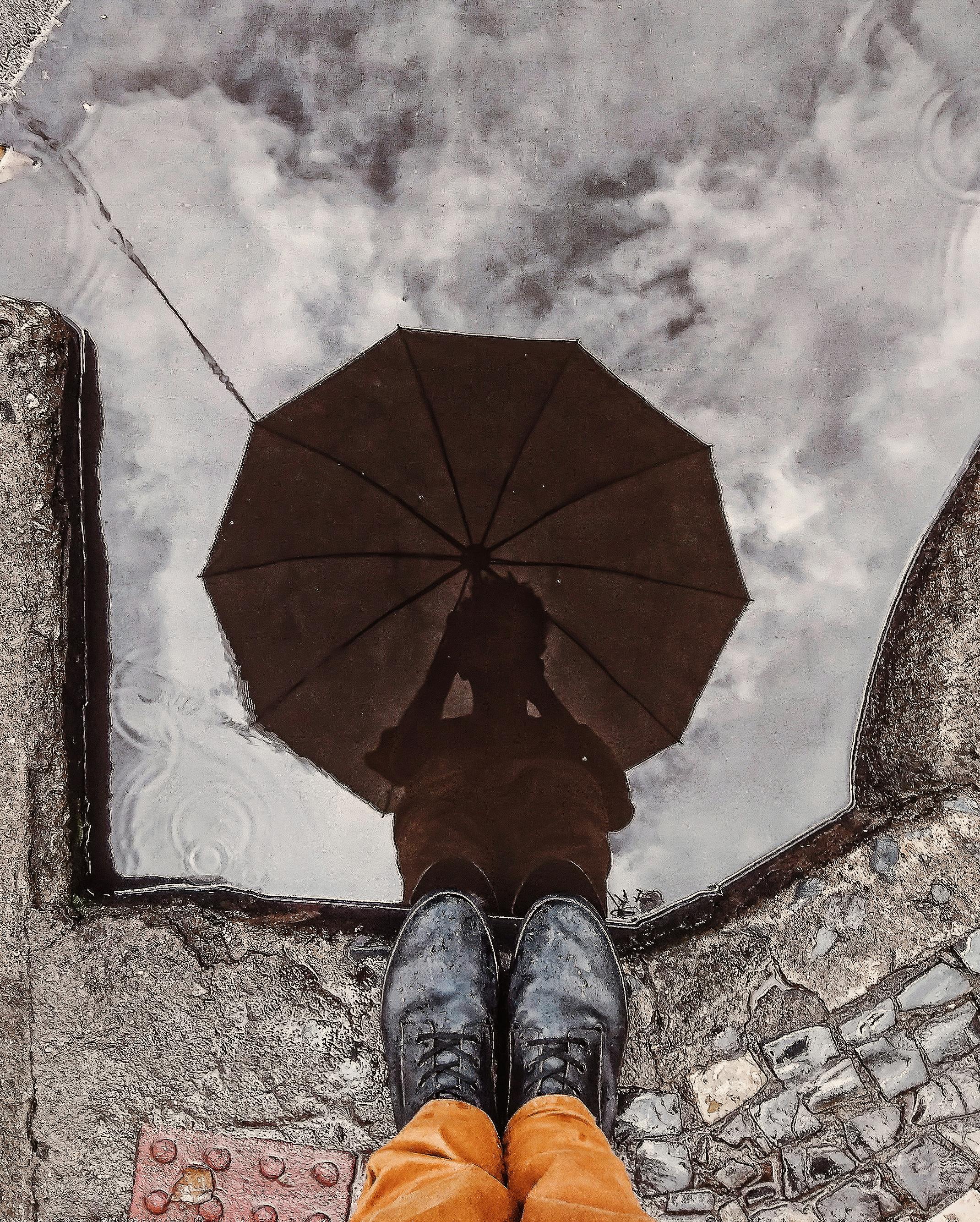 城市环境中，一个人撑着伞的倒影，被创造性地捕捉在水坑里