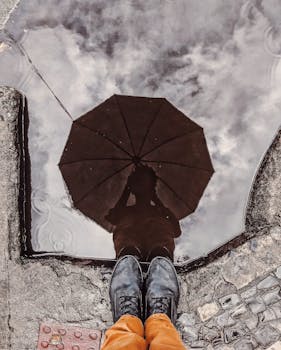 城市环境中，一个人撑着伞的倒影，被创造性地捕捉在水坑里