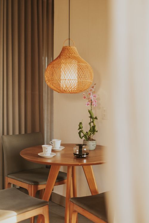 Free Comfortable dining setup with woven pendant light, wooden table, and orchid in serene ambiance. Stock Photo