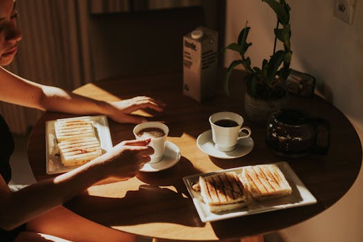 Warm morning light on coffee and grilled sandwiches in a cozy indoor setting.