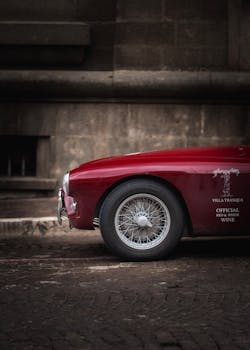 Elegant side view of a classic red sports car on a cobblestone street, with stone wall background.
