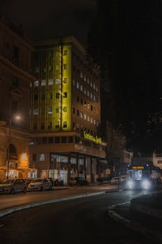 A nighttime urban scene featuring a brightly lit building and street traffic.