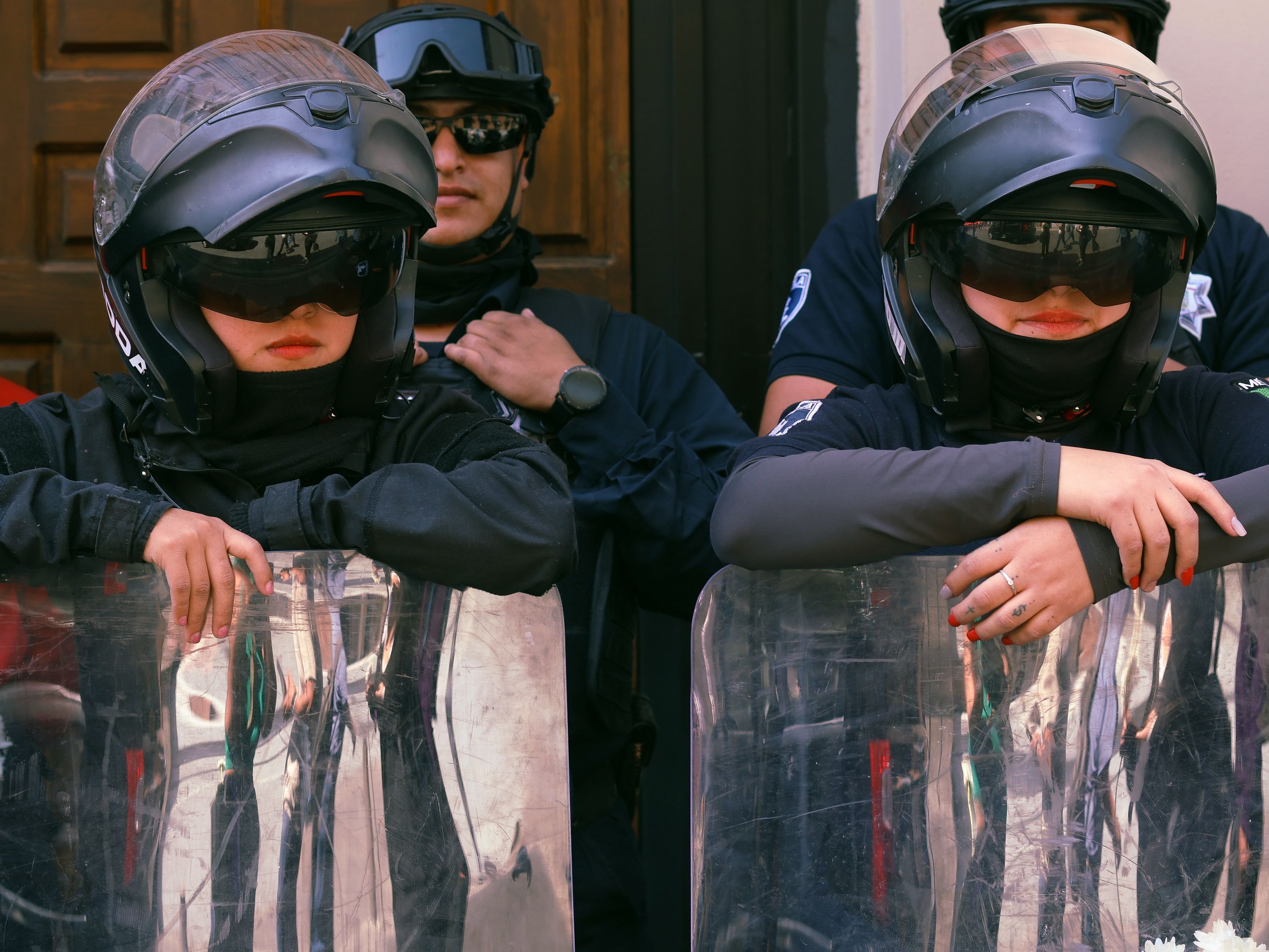 Group of police officers in full riot gear standing on duty outdoors.