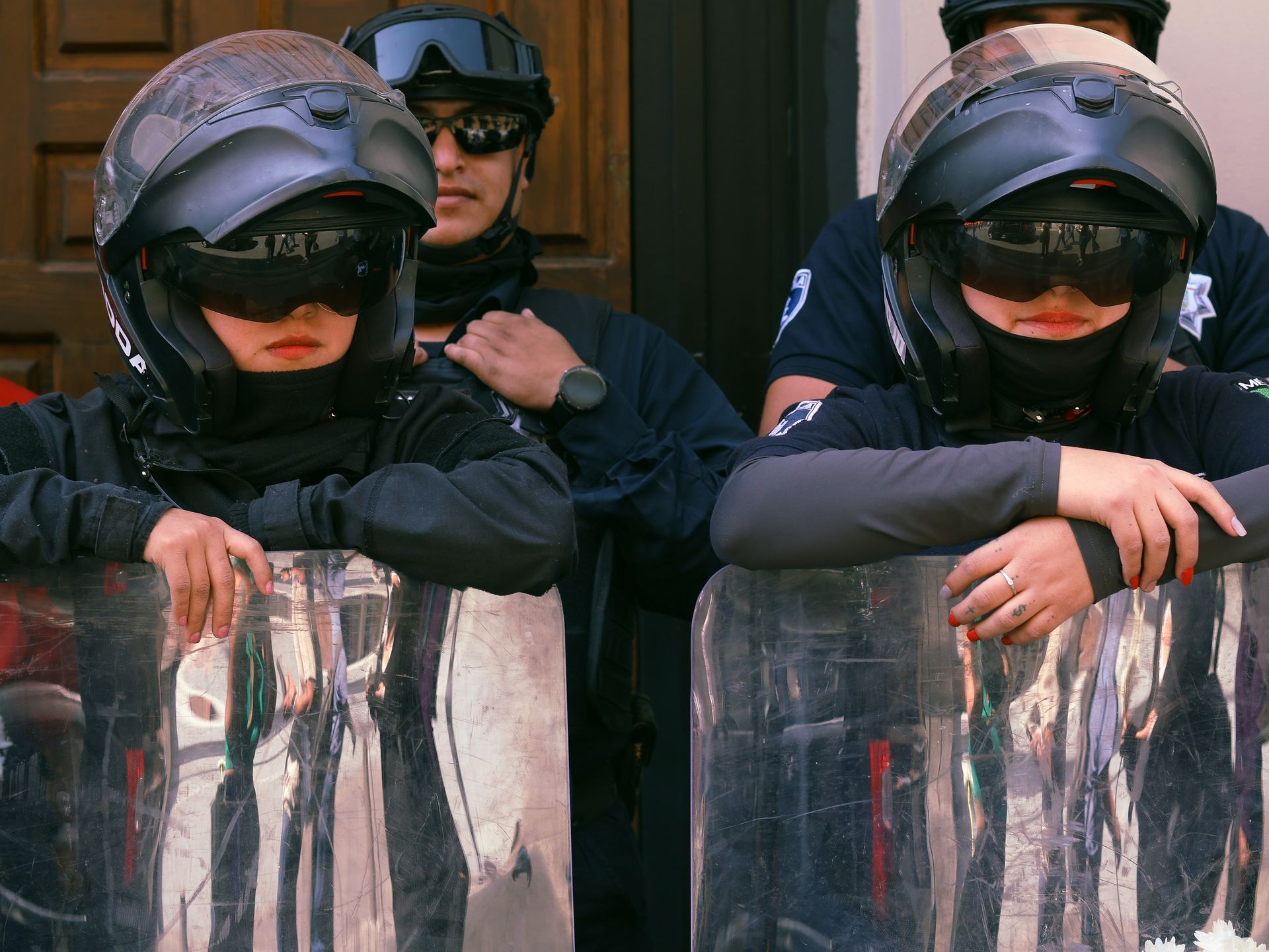 Group of police officers in full riot gear standing on duty outdoors.