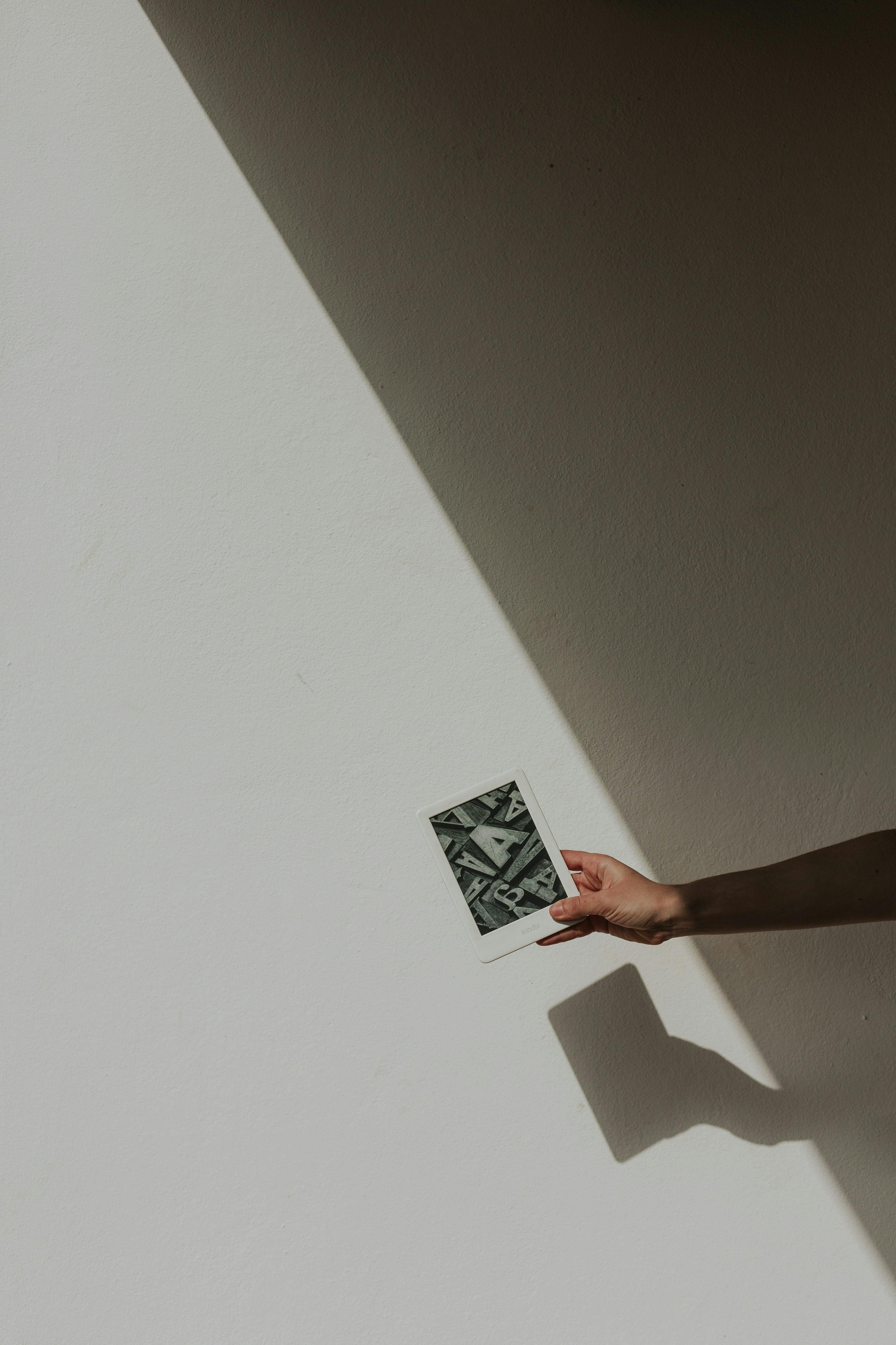 A hand holding a Polaroid against a shadowed white wall, showcasing minimalist aesthetics.