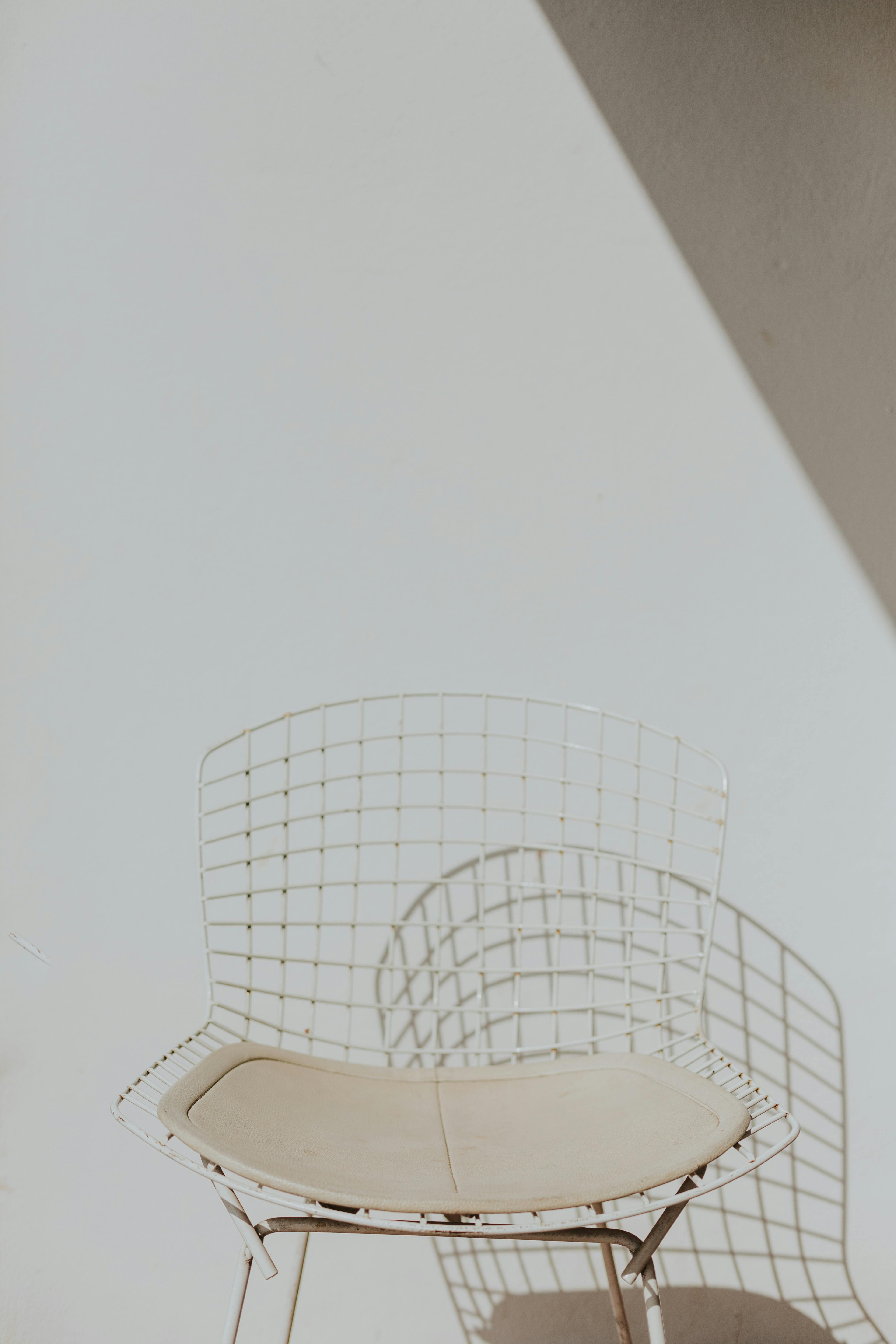 A minimalist wire chair casts a geometric shadow on a plain wall.