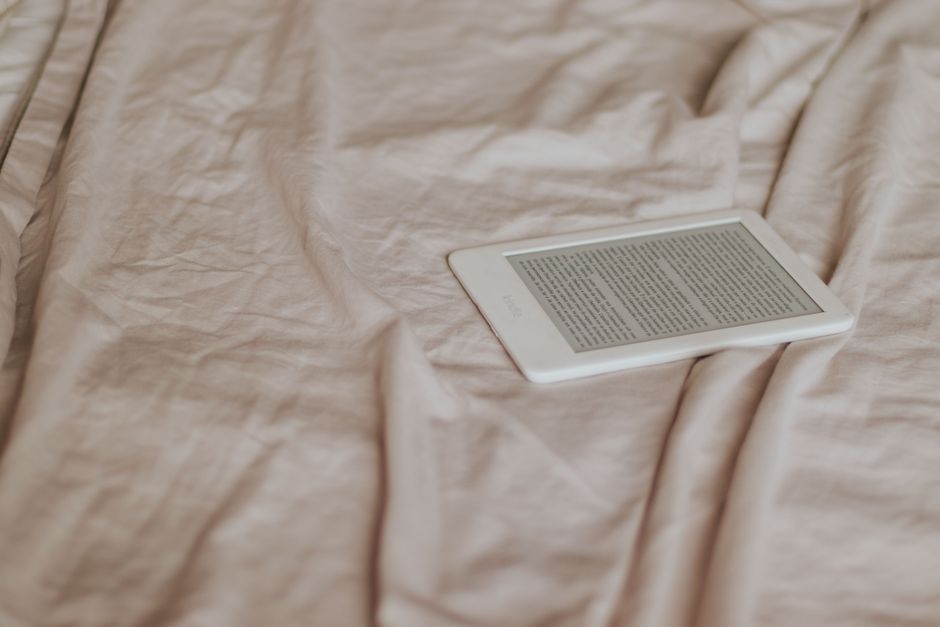 Fotomural Un lector digital minimalista descansando sobre un edredón beige arrugado, evocando un ambiente acogedor para la lectura.