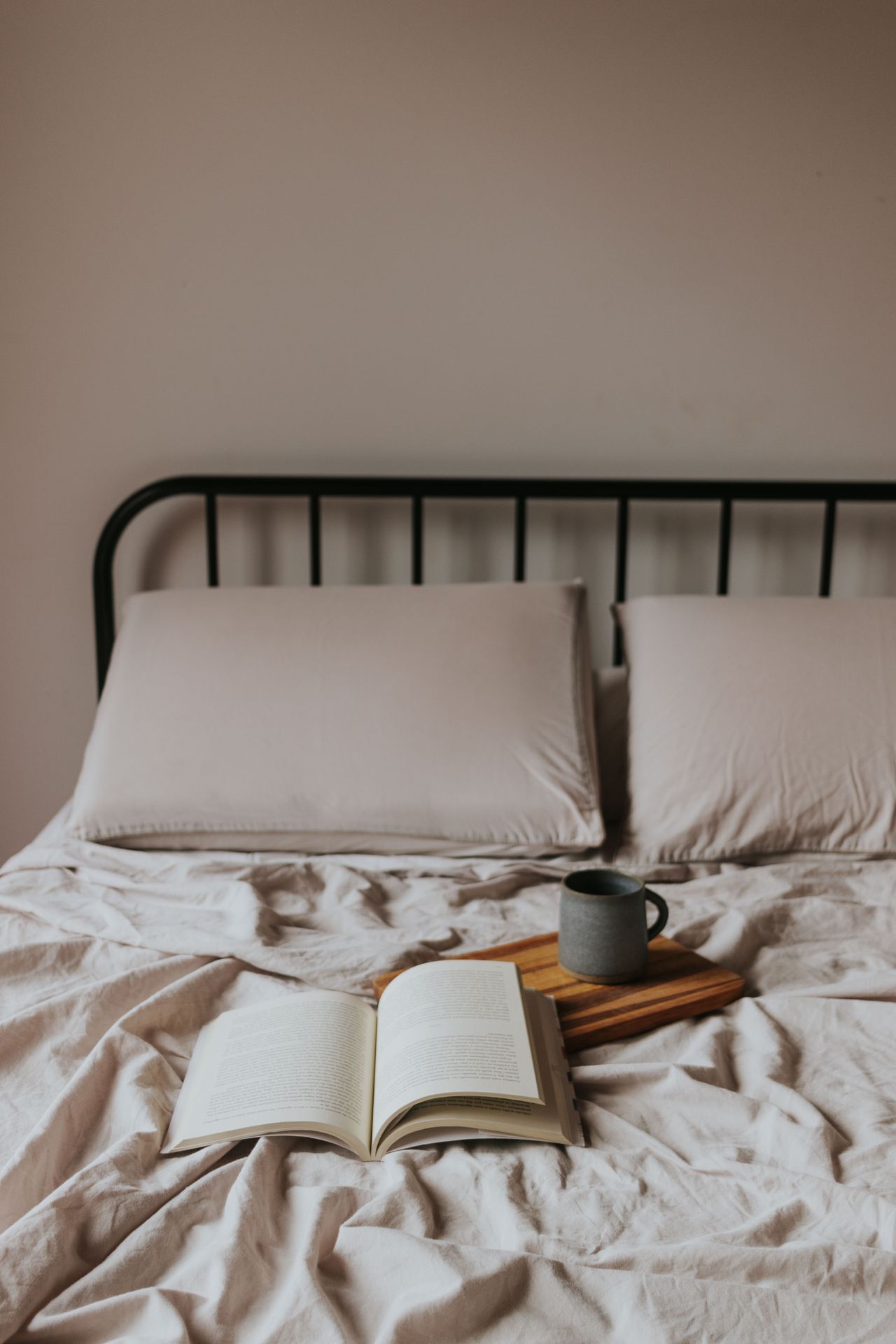 Open book and coffee mug on a wooden tray on rumpled beige bedding