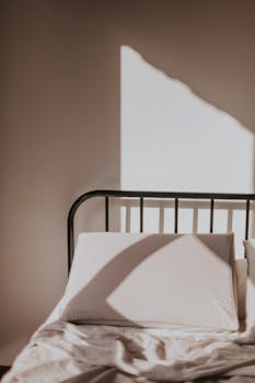A minimalist bed with sunlight casting geometric shadows across the sheets and pillow.
