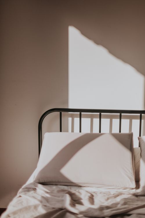 Free A minimalist bed with sunlight casting geometric shadows across the sheets and pillow. Stock Photo