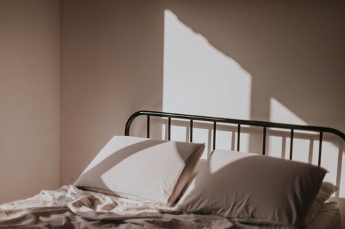 Free Soft morning light casts shadows on a neatly made bed with a metal headboard. Stock Photo