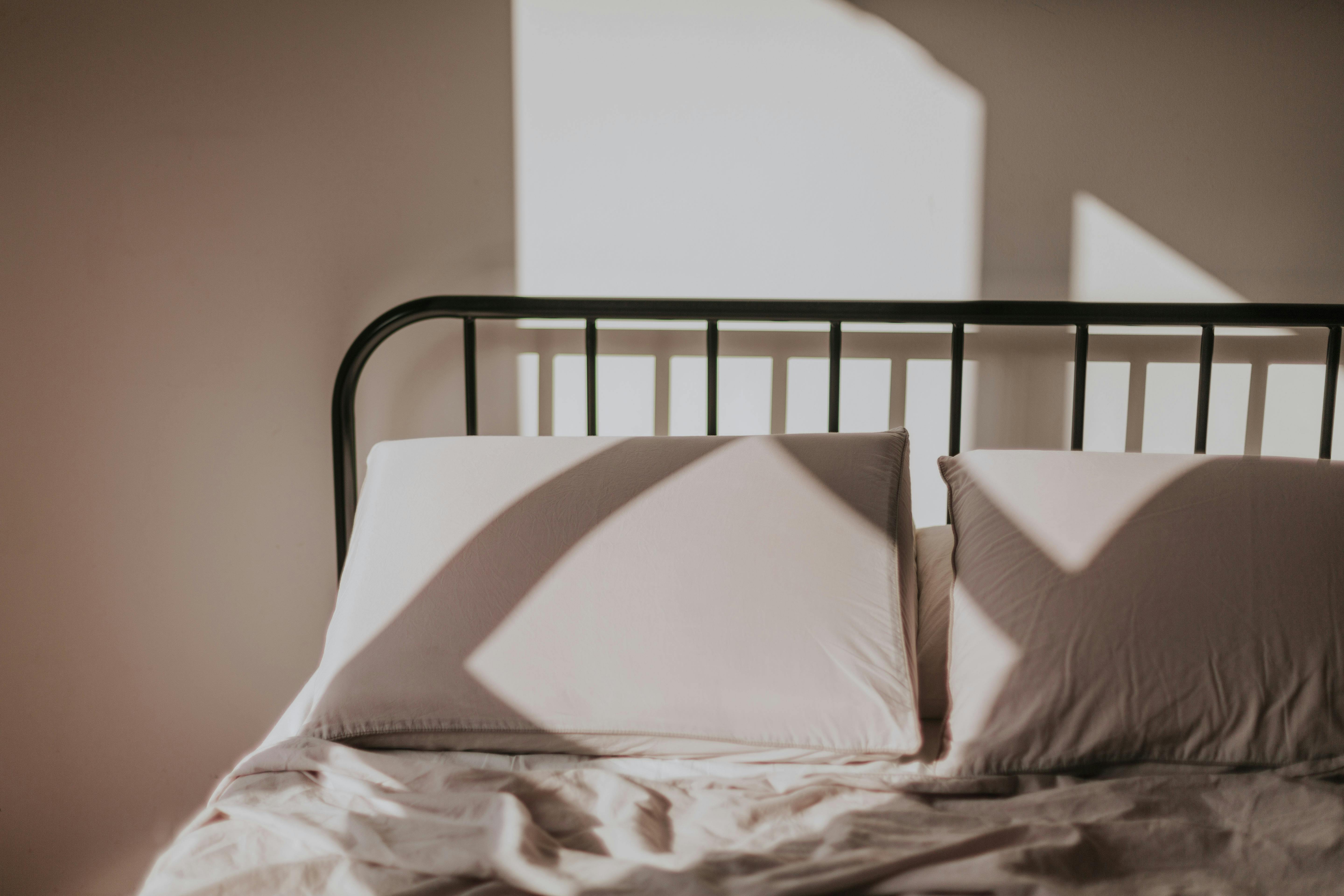 Sunlight casting geometric shadows on a bed with pillows, creating a serene morning atmosphere.