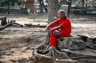 在印度尼西亚万丹，一名身穿红色服装的老年男子正坐在树根上休息