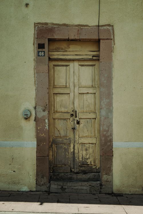 Free A rustic wooden door with peeling paint on an aged building facade. Stock Photo