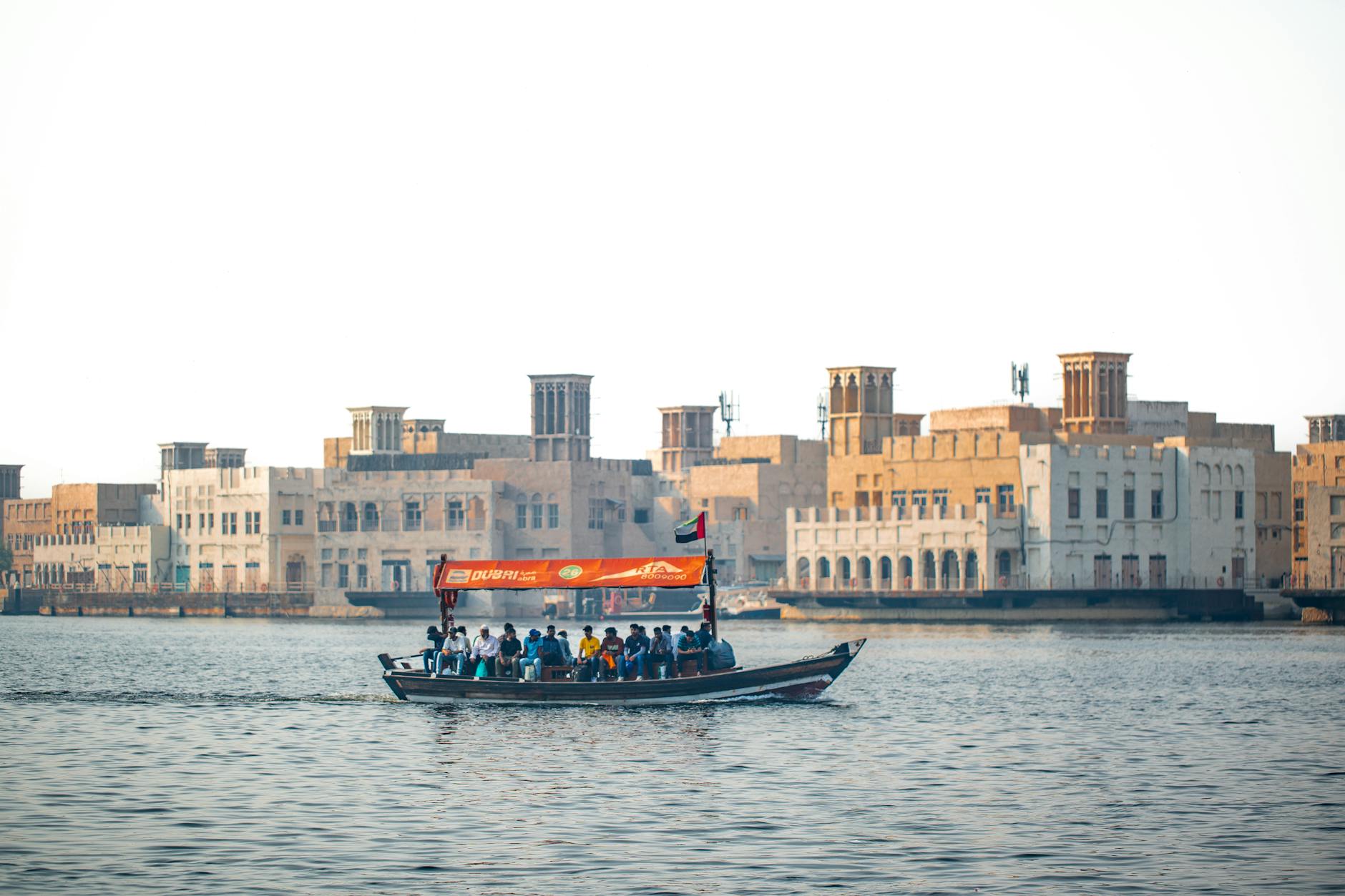 Traditional boat crossing Dubai Creek with historical architecture in the backdrop.