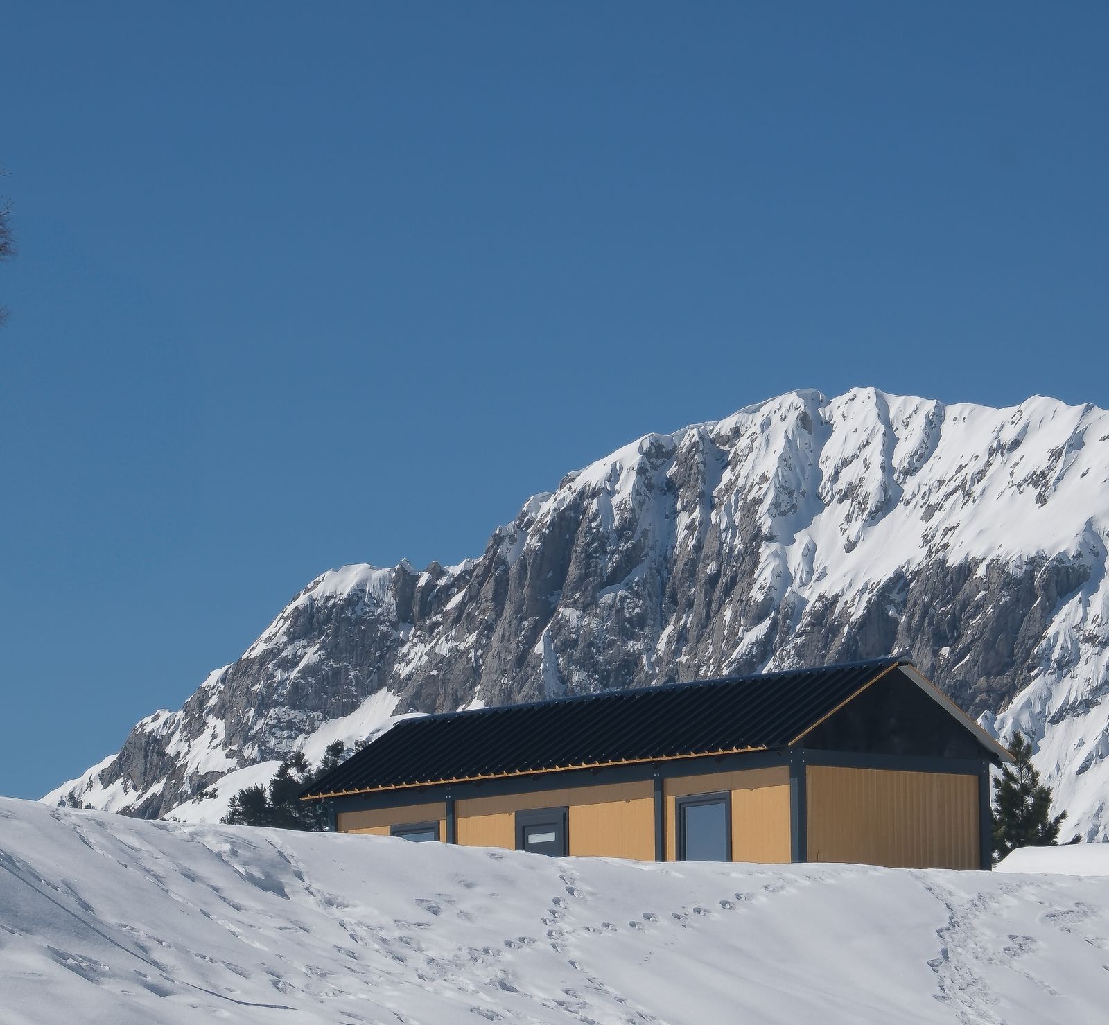 Wooden cabin on a snowy slope beneath a jagged, snow-covered mountain ridge in Shkodër County, Albania