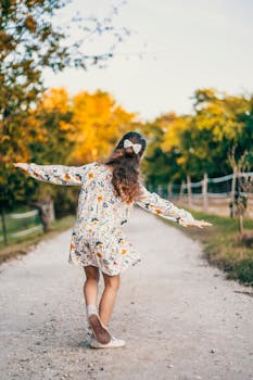 一个女孩无忧无虑地在风景如画的土路上旋转，四周环绕着鲜艳的秋叶