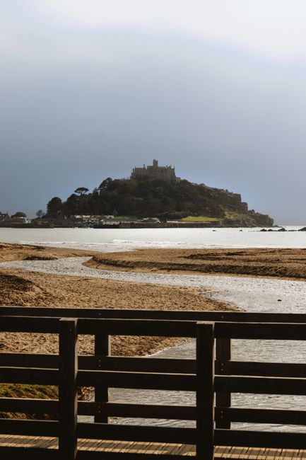 View of St Michael's Mount in England from a seaside beach with cloudy sky.