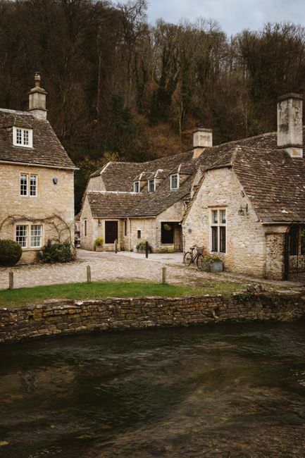 Tranquil scene of historic stone cottages by a river in the Cotswolds, England.