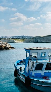 Blue boat on serene waters with rocky coastline in Latakia, Syria.