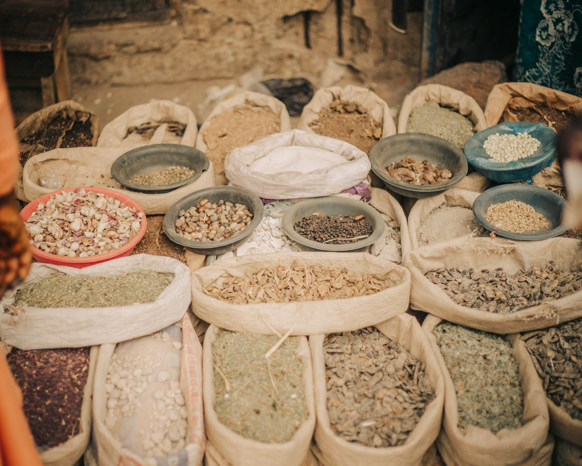 Bags and bowls filled with diverse dried herbs and spices displayed at an outdoor market.