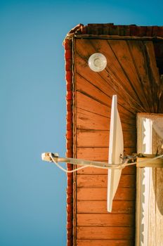 Close-up of a rustic wooden rooftop featuring a satellite dish against a clear blue sky. Warm tones and textures.